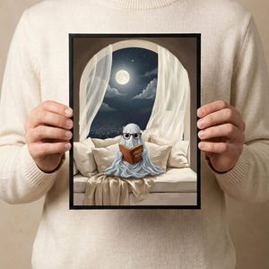 The moonlit bed ghost reading print held in both hands by a person in a cream sweater, showing its scale