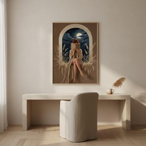 The moonlit reading print framed above a restrained pale desk beside a soft armchair