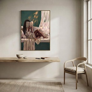 Gold-framed emerald green art print of a Black woman reading on a window seat above a floating oak shelf with two bowls and a woven chair in a bright minimal room.