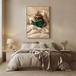 The framed sloth print above a bed with linen bedding and a taupe throw, beside a lamp and a small vase of dried flowers