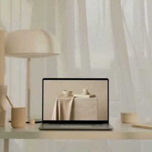 Puede incluir: Un ordenador port&aacute;til sobre un escritorio con una l&aacute;mpara beige y un portal&aacute;pices beige acanalado. La pantalla muestra una tela beige drapeada sobre un bloque con un cuenco peque&ntilde;o y una vela. La paleta de colores es monocrom&aacute;tica y neutra.