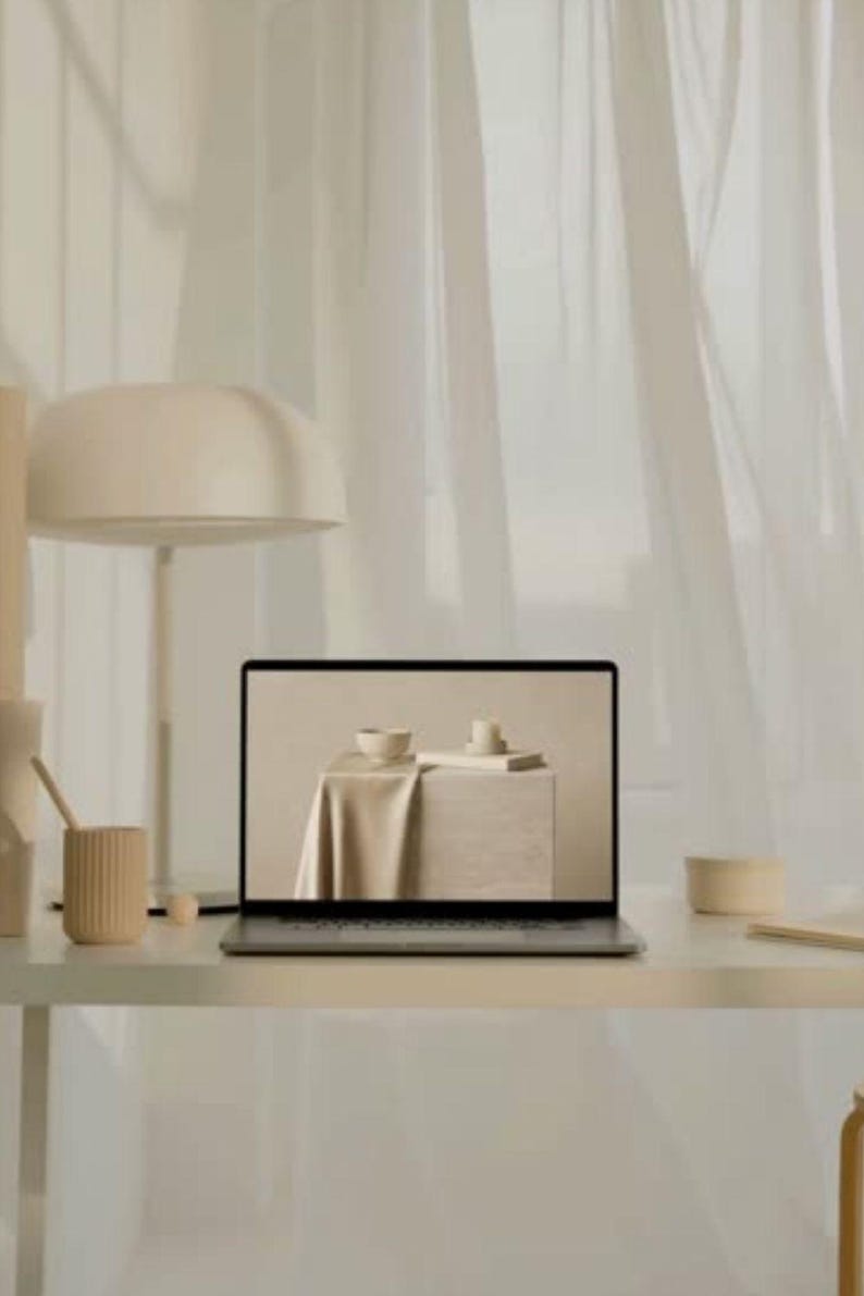 Puede incluir: Un ordenador port&aacute;til sobre un escritorio con una l&aacute;mpara beige y un portal&aacute;pices beige acanalado. La pantalla muestra una tela beige drapeada sobre un bloque con un cuenco peque&ntilde;o y una vela. La paleta de colores es monocrom&aacute;tica y neutra.