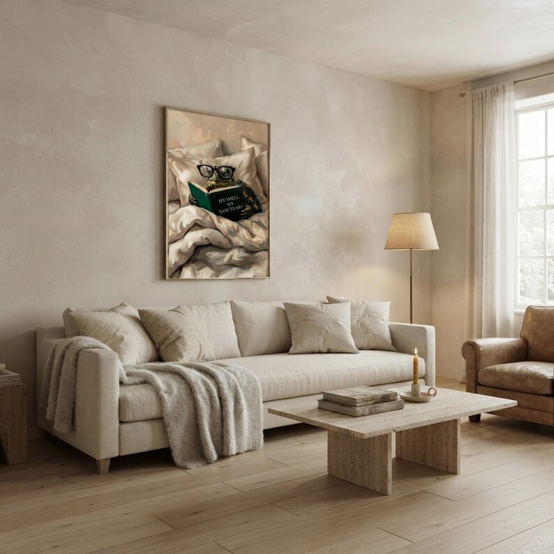 The tortoise reading print framed above a cream sofa in a sunlit living room with an armchair, a travertine coffee table and a floor lamp