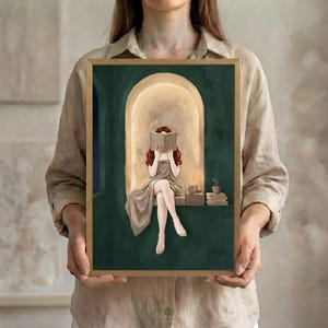 The red-haired woman reading in an emerald green arched nook art print in a thin gold frame, held up in both hands to show its size.