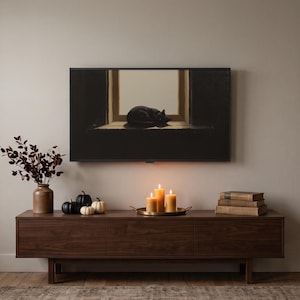 Puede incluir: Un mueble multimedia largo de nogal sostiene un jarrón marrón con follaje oscuro, tres calabazas pequeñas, una bandeja de latón con tres velas encendidas y tres libros apilados. Arriba, un televisor de pared muestra un gato negro durmiendo.