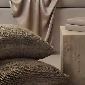 Close-up detail from Alcove Reading Wall Art, a cropped fragment of the printable artwork: a satin throw falling over the window seat, textured boucle floor cushions and a raw wood stool with two stacked books.