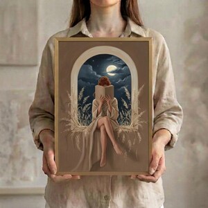 A person holding the framed moonlit reading print, showing its scale against the body