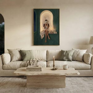 Emerald green reading nook art print above a deep cream sofa in an airy plaster living room, with a travertine coffee table, a lit candle and an arched doorway to a garden.