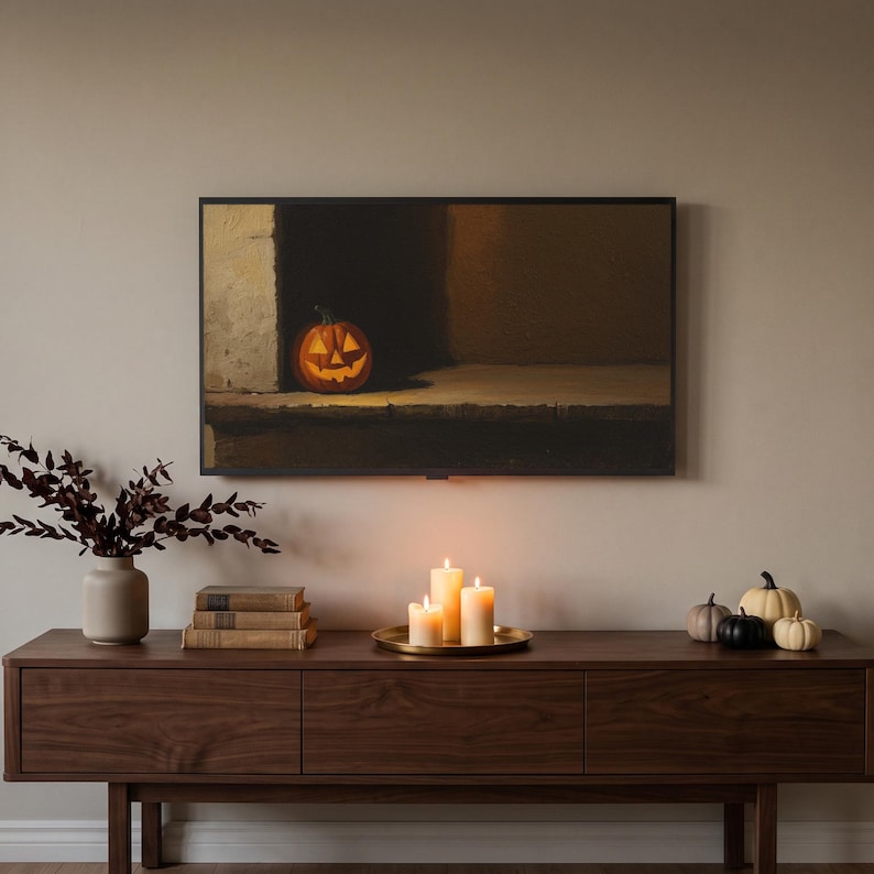 Lantern on a step art from the set on a Frame TV in a late-October living room above a walnut console, with lit pillar candles, black and cream pumpkins, dried branches and an armchair