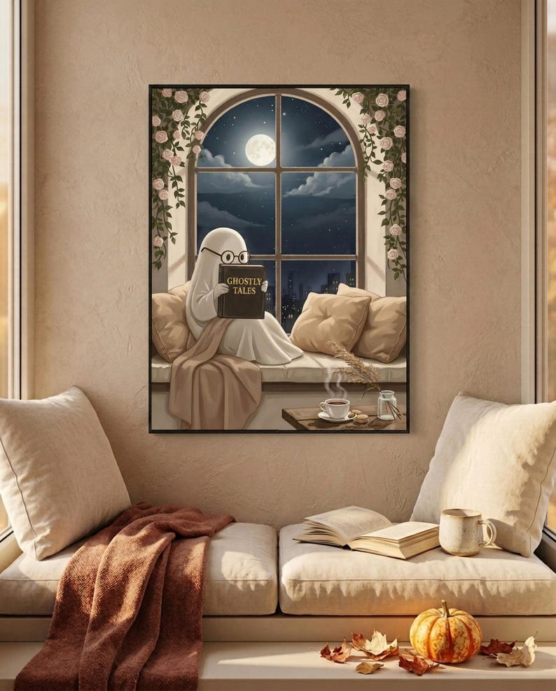 Painterly print of a small ghost in round glasses reading on a window seat with a cup of coffee, holding a book titled Ghostly Tales, framed above a cushioned window bench with a wool throw and a small pumpkin