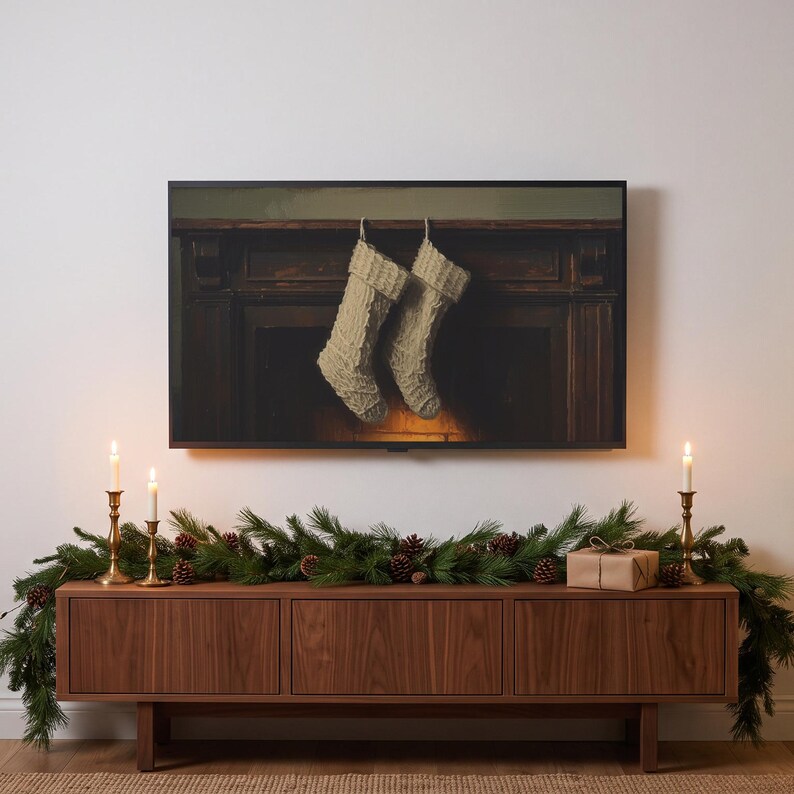 Stockings on a mantel art from the set on a Frame TV in a Christmas living room, above a walnut console with pine garland, lit brass candlesticks and a wrapped parcel