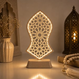 May include: A light-coloured, sandal-shaped decorative lamp featuring an intricate, laser-cut geometric star pattern. The lamp is mounted on a solid rectangular base and emits a warm, soft glow through the cutouts, illuminating the surrounding area.