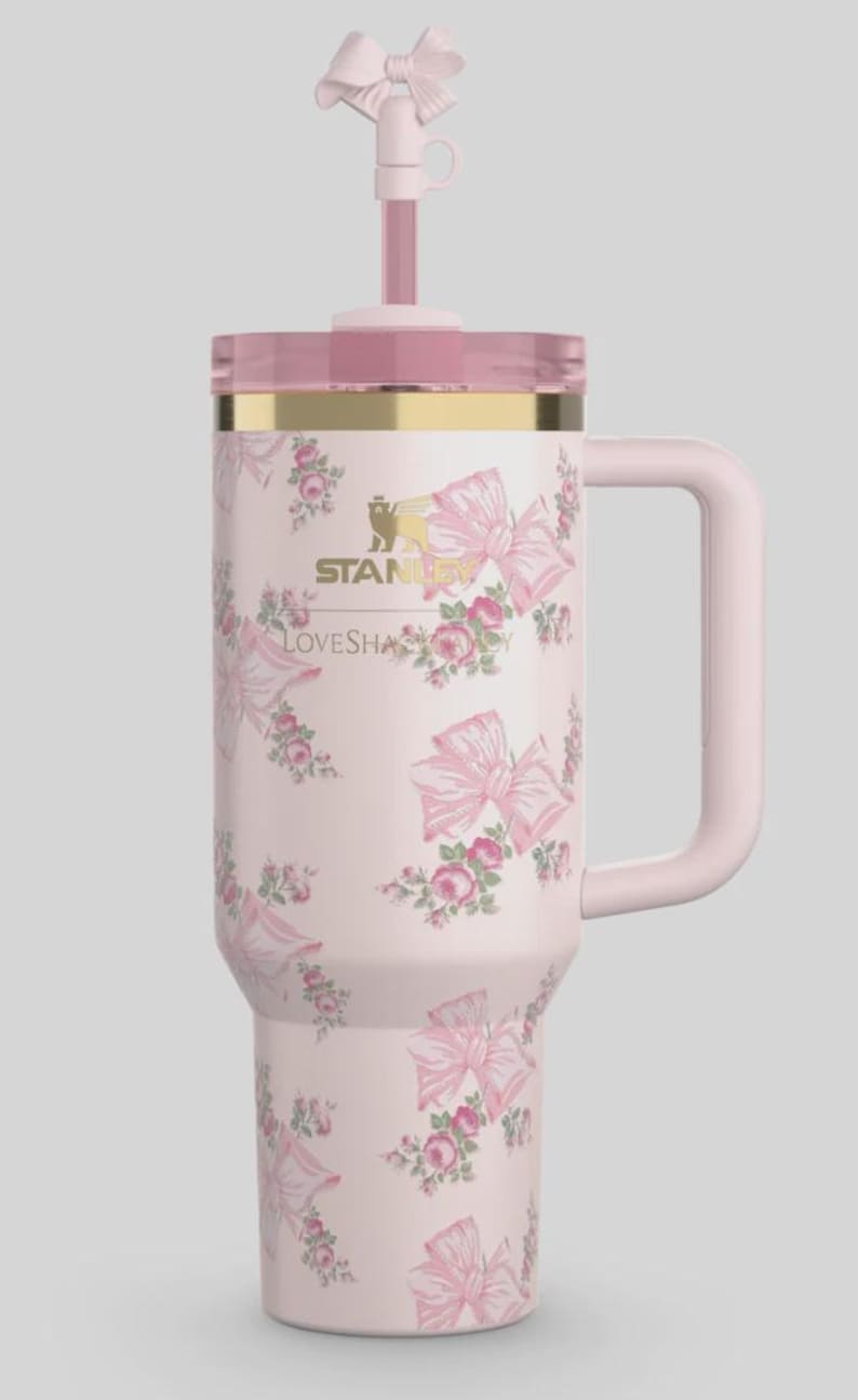 May include: A pink insulated tumbler with a handle, lid, and straw, decorated with a floral and bow pattern. The tumbler features the "Stanley" and "LOVESHAPE" logos. The straw is topped with a bow.