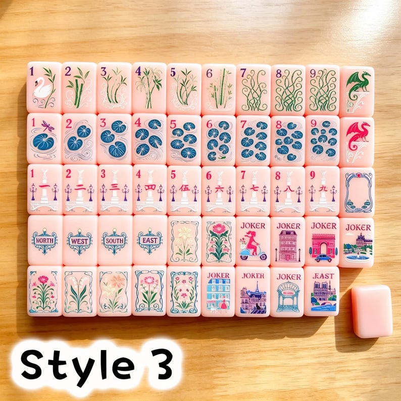 May include: A set of light pink Mahjong tiles featuring various illustrations including numbers one through nine, dragons, compass directions, flowers, and Parisian landmarks. Each tile displays detailed colorful graphics and text labels.