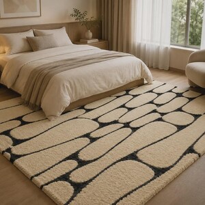 Puede incluir: Una alfombra rectangular de pelo largo en color crema con un patr&oacute;n repetitivo de formas redondeadas similares a guijarros, delineadas con l&iacute;neas de color gris carb&oacute;n oscuro. La alfombra cubre una gran parte del suelo con su textura.