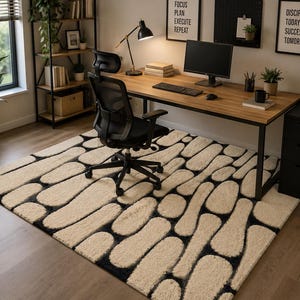 Puede incluir: Una alfombra rectangular con un patr&oacute;n de alto contraste de formas redondeadas de color crema, similares a guijarros, separadas por canales de color negro intenso. La alfombra est&aacute; colocada sobre un suelo de madera bajo un escritorio.