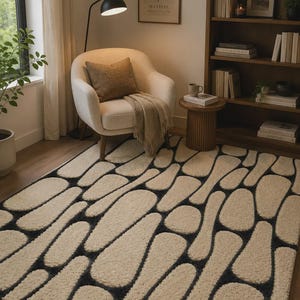 Puede incluir: Una alfombra rectangular con un patr&oacute;n de guijarros de pelo largo en color crema sobre un fondo gris carb&oacute;n oscuro. El dise&ntilde;o consiste en formas redondeadas e irregulares que crean un aspecto texturizado y org&aacute;nico en toda la superficie.