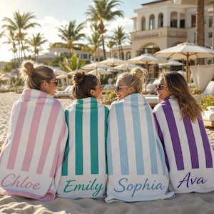 Puede incluir: Cuatro toallas de playa con rayas verticales en rosa, turquesa, azul claro y morado, cada una con una franja blanca y un nombre bordado en la parte inferior en letra cursiva: Chloe, Emily, Sophia y Ava, respectivamente.