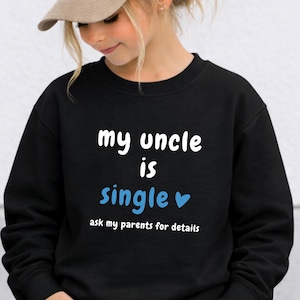 May include: A black long-sleeve sweatshirt featuring white text that reads my uncle is, the word single in light blue with a small blue heart, and the text ask my parents for details in white. The sweatshirt has a crew neckline and ribbed cuffs.