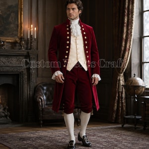 Op de afbeelding: Een bordeauxrood fluwelen driedelig pak met gouden knopen. De lange jas, het vest en de knielange broek worden gecombineerd met een wit gerimpeld overhemd en kousen. De outfit doet denken aan historische formele kleding.