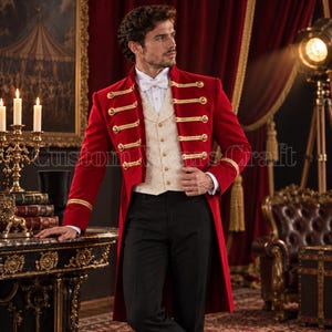 Op de afbeelding: Een rode pandjesjas met gouden vlechtwerk en metalen knopen, gedragen over een crèmekleurig vest met patroon, een wit overhemd met kraag, een witte vlinderdas en een zwarte broek. Het ensemble heeft lange mouwen met gouden details bij de manchetten.