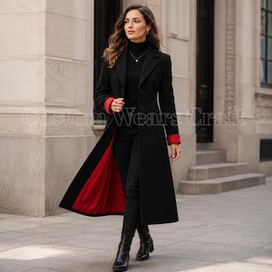 Op de afbeelding: Een lange zwarte jas met een felrode binnenvoering en rode manchetten, gedragen over een zwarte coltrui en een zwarte broek. De jas heeft een gestructureerde kraag, knoopsluitingen en de tekst Custom Wears Craft is zichtbaar.