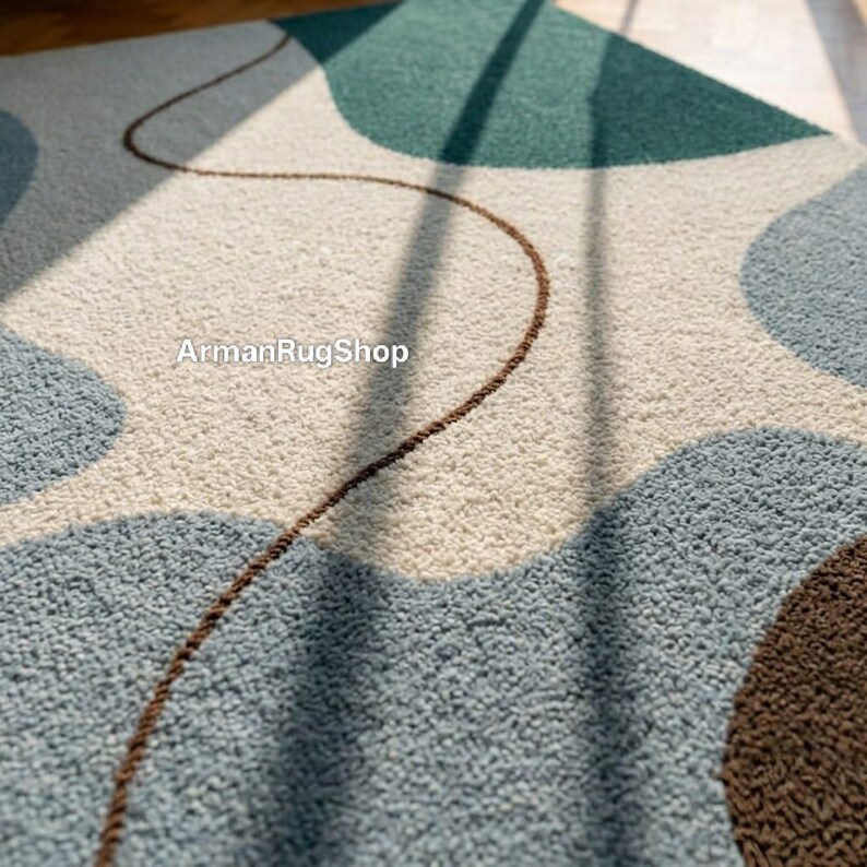 May include: A close-up of a modern area rug with a textured surface. The rug features a pattern of overlapping shapes in shades of blue, green, cream, and brown. A thin brown line meanders across the rug. The text "ArmanRugShop" is visible.