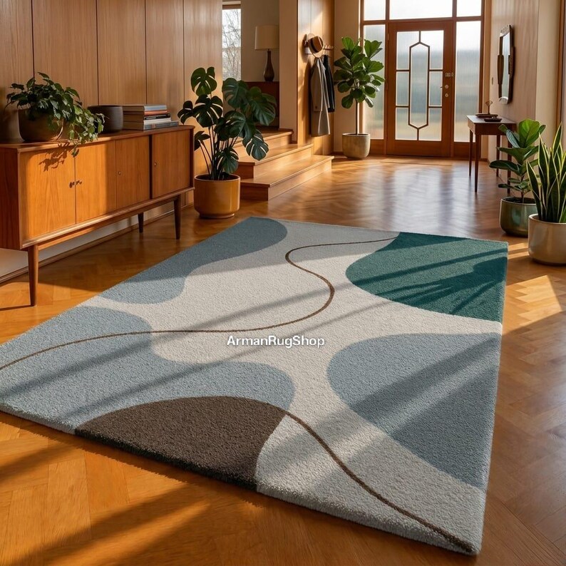 May include: A rectangular area rug with an abstract design in shades of blue, green, and brown. The rug features a light beige background with organic shapes and a curved brown line. The rug is placed on a wooden floor.