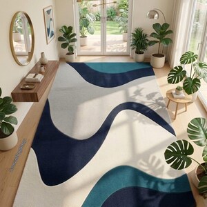 May include: A rectangular area rug featuring a large-scale abstract pattern of flowing, organic waves in shades of deep navy blue, teal, and off-white. The rug is positioned on a light wood floor in a room filled with various potted green plants.