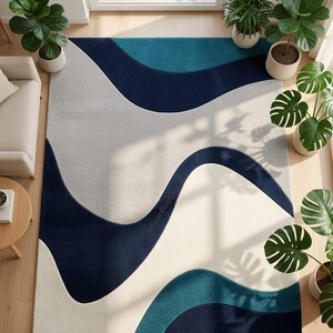 May include: A rectangular area rug featuring a flowing, abstract wave pattern in shades of deep navy blue, teal, and off-white. The design consists of large, curved colour-blocked sections. The text ArmanRugShop is printed in small letters on the rug.