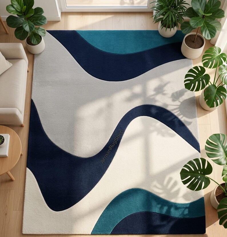 May include: A rectangular area rug featuring a flowing, abstract wave pattern in shades of deep navy blue, teal, and off-white. The design consists of large, curved colour-blocked sections. The text ArmanRugShop is printed in small letters on the rug.