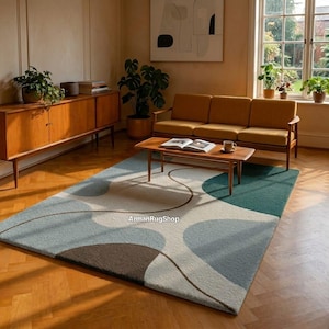 May include: A modern area rug with a geometric design in shades of blue, gray, and brown. The rug features a curved pattern and is placed in a living room setting with a wooden coffee table and sofa. The rug's dimensions are not visible.