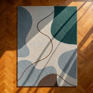 May include: A rectangular rug with an abstract design. The rug features a pattern of overlapping shapes in shades of blue, green, and brown against a cream background. A thin, brown line meanders across the surface. The text "ArmanRugShop" is visible.