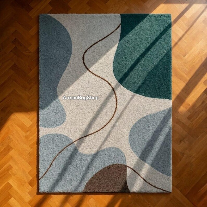 May include: A rectangular rug with an abstract design. The rug features a pattern of overlapping shapes in shades of blue, green, and brown against a cream background. A thin, brown line meanders across the surface. The text "ArmanRugShop" is visible.