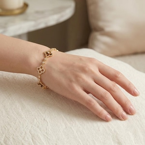May include: A gold-toned chain bracelet featuring a series of four-leaf clover motifs. Each clover is outlined with small, clear, sparkling stones and contains a dark, smooth, brown inlay at the center, connected by a delicate gold-toned metal chain.