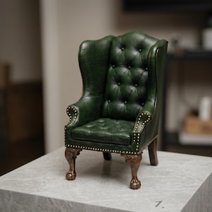 Könnte beinhalten: Miniatur-Ledersessel in Grün mit hohem Rücken und Knopfheftung. Der Stuhl hat verzierte, bronzefarbene Beine und ist mit kleinen Messingstiften an den Kanten besetzt. Ein klassisches, elegantes Stück.