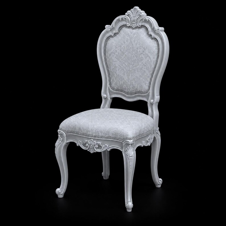 May include: A white wooden chair featuring an ornate carved frame with scrollwork details. The backrest and seat are upholstered in a light gray fabric with a subtle, intricate damask pattern. The chair stands on four curved cabriole legs.