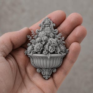 May include: A miniature gray wall-mounted planter featuring an ornate, scroll-work backplate and a fluted basin. The planter is filled with a detailed arrangement of sculpted flowers, including roses and small blossoms, all in a uniform gray finish.