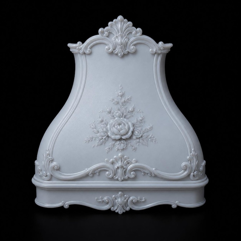 May include: A light gray range hood featuring an ornate, raised floral relief design at the center. The structure has a curved silhouette with intricate scrollwork detailing along the top crest and the bottom edge, finished in a smooth, matte surface.