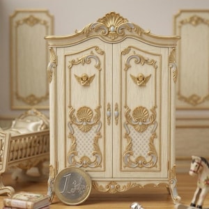 May include: A miniature cream-colored armoire with ornate gold detailing, including cherub accents and shell-shaped designs. The two-door cabinet features a classic, elegant style, with a coin in front for scale. The armoire is part of a dollhouse furniture set.