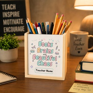 May include: A light-colored wooden pencil holder filled with various pens and pencils. The front features the text "Books Brains and Beautiful Chaos" in colorful letters, along with small illustrations of books and stars, and a "Teacher Name" label.