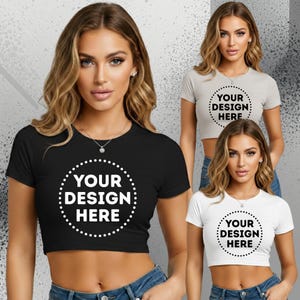 May include: Three short-sleeved crop tops in black, light grey, and white. Each shirt features a circular dotted frame with the text "YOUR DESIGN HERE" printed in the centre. The garments are fitted with a crew neckline and a cropped hemline.