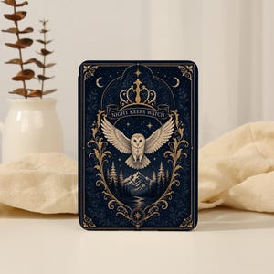Op de afbeelding: Een rechthoekige e-reader hoes met een donkerblauwe achtergrond en gouden filigraanranden. In het midden staat een witte uil met gespreide vleugels boven een berg- en boslandschap. De tekst NIGHT KEEPS WATCH staat op een banier.