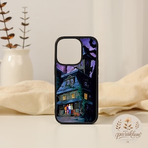 May include: A black phone case featuring a graphic illustration of a spooky, multi-story house at night with a purple sky. Four cartoon characters and a dog stand near the front entrance of the house, which has glowing yellow windows.