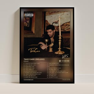 May include: A framed poster of the Drake album Take Care (Deluxe) featuring a dark, moody photograph of the artist with a candle and gold accents. The print includes the tracklist, a Parental Advisory label, and a Spotify code on a black background.