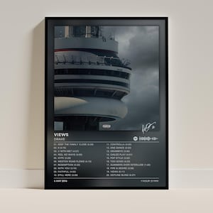 May include: A framed poster of the Drake album Views, featuring a photograph of the CN Tower against a cloudy sky. The print includes the album title, artist name, a tracklist of twenty songs with durations, a Spotify code, and a signature.