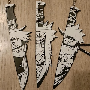 Può includere: Tre portachiavi in bianco e nero in stile anime, ciascuno progettato come un coltello con illustrazioni di personaggi. I portachiavi hanno attacchi argentati. I personaggi sono raffigurati con tratti del viso e acconciature dettagliate.