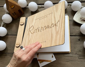 May include: A wooden photo album with a black spine and two metal clasps. The front cover is engraved with the text "Congratulations on your Retirement".