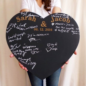 K&ouml;nnte beinhalten: Eine schwarze herzf&ouml;rmige Tafel mit den Namen Sarah und Jacob in goldenen Lettern. Das Datum 06.12.2014 ist unter den Namen geschrieben. Die Tafel ist mit wei&szlig;er Kreide beschriftet, darunter Gl&uuml;ckw&uuml;nsche f&uuml;r das Paar.