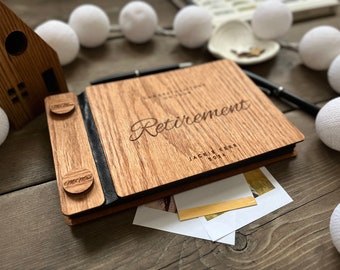 May include: A wooden photo album with a black leather spine and two wooden clasps. The album is engraved with the words "Retirement" and "Jackie Kerr 2024".